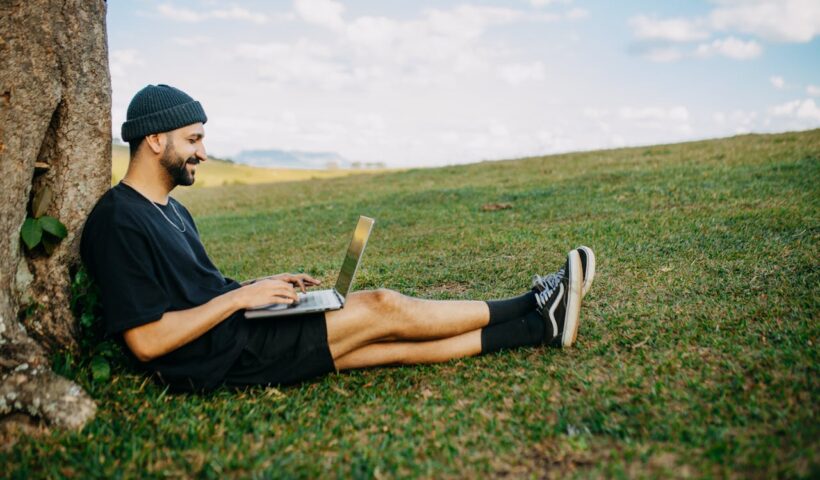 A man sitting in a rural outside area working on a laptop.