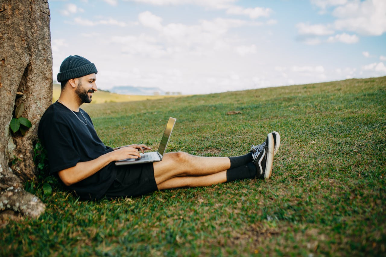 A man sitting in a rural outside area working on a laptop.