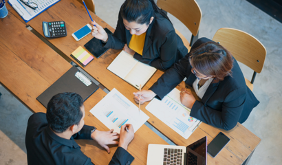 A team of three sits at a table poring over data and research reports.