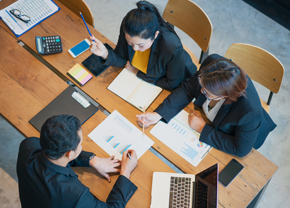 A team of three sits at a table poring over data and research reports.