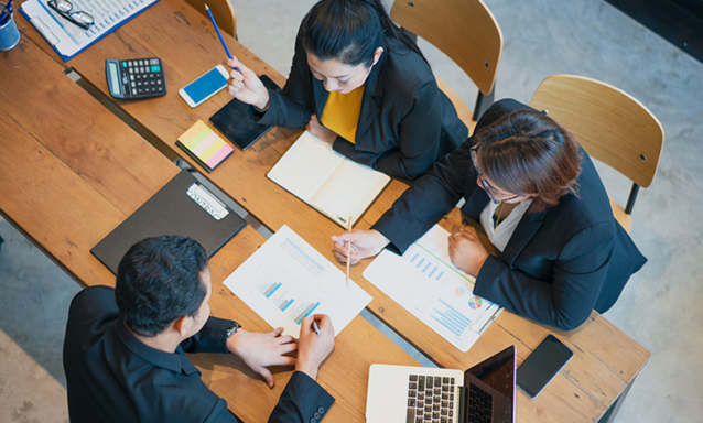 A team of three sits at a table poring over data and research reports.